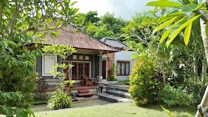 Une maison traditionnelle avec un toit en tuiles, un petit porche et un jardin agrémenté d’un élément décoratif aquatique.