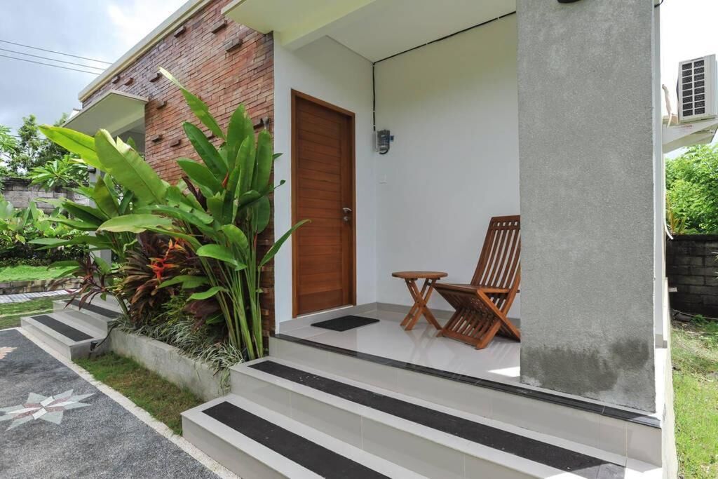 Uma casa com fachada de tijolos, porta de madeira e varanda com uma cadeira e uma mesa pequena.