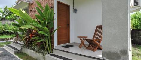 Uma casa com fachada de tijolos, porta de madeira e varanda com uma cadeira e uma mesa pequena.