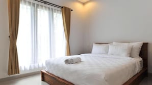 Une chambre d’hôtel moderne avec un grand lit, une tête de lit en bois et une vue sur l’extérieur à travers des rideaux transparents.