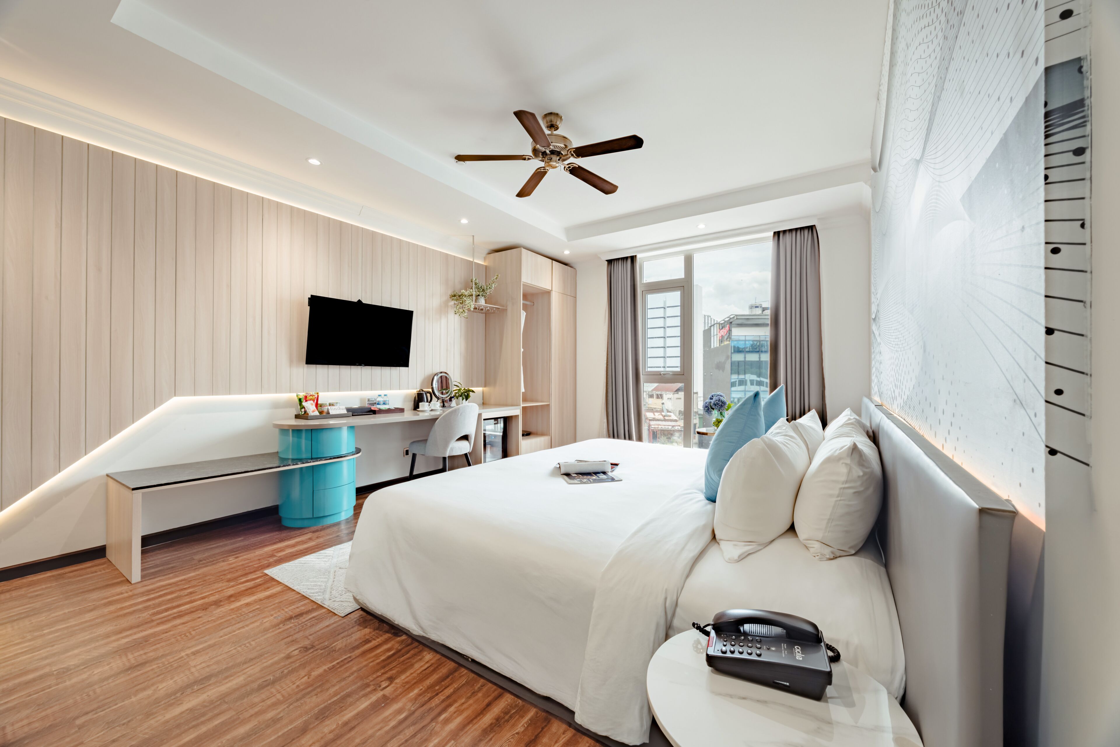 Una habitación de hotel moderna con una cama grande, un escritorio, un televisor de pantalla plana y un ventilador de techo.