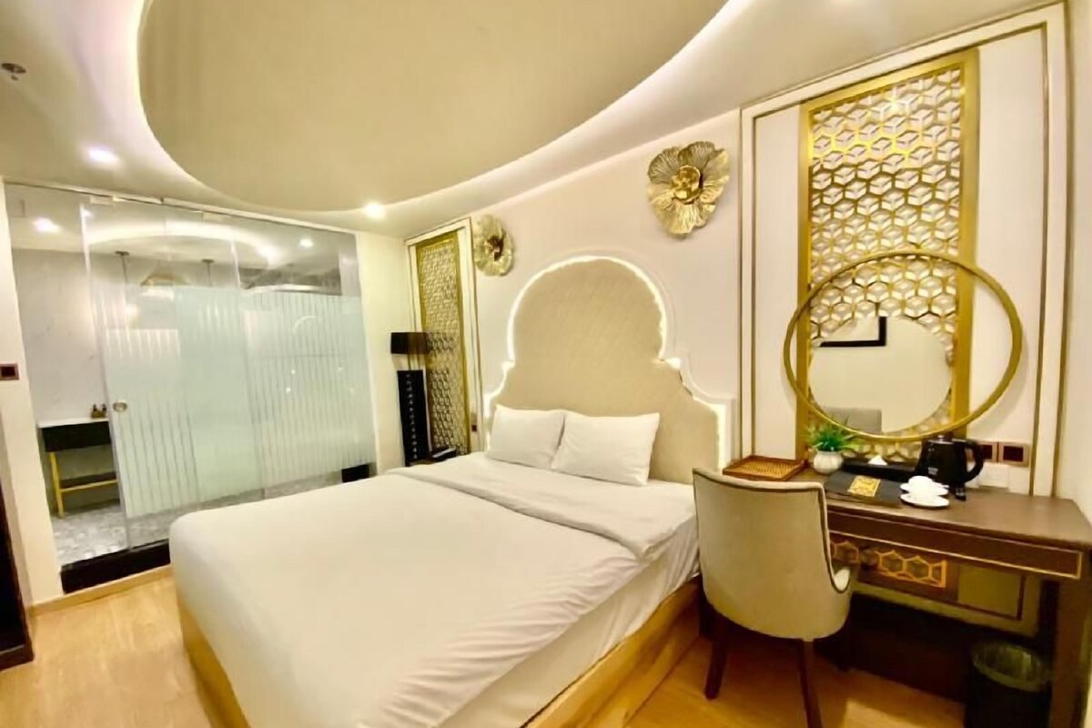 Una habitación de hotel moderna con una cama grande, un escritorio con una silla, un espejo redondo y un panel decorativo en la pared.