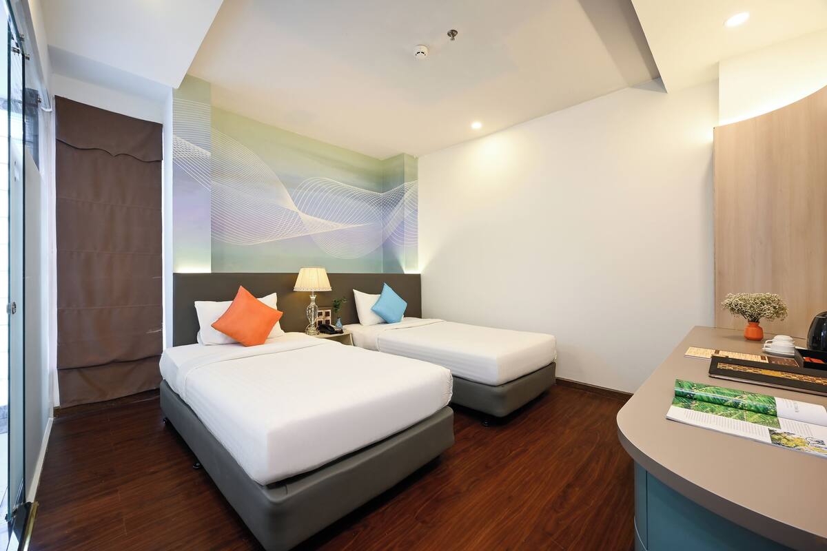 A hotel room with two beds, a desk, and a large window.