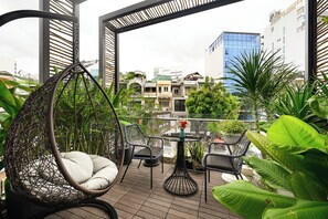 Un balcon agrémenté d’un fauteuil suspendu, d’une table ronde et de chaises, le tout entouré d’une végétation luxuriante.