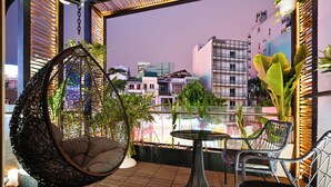 A balcony with a hanging chair, a small table, and chairs, overlooking a cityscape with buildings and a view of the sky. - Cicilia Saigon Center (Ho Chi Minh City)