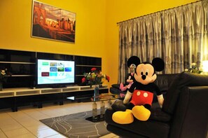 Un salon avec un grand téléviseur à écran plat, un doudou à l’effigie de Mickey Mouse et un tableau accroché au mur.