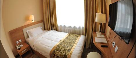 A hotel room with a bed, a desk, a TV, a lamp, and a window with curtains.