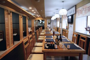 Um restaurante com mesas e cadeiras de madeira compridas e luminárias pendentes.