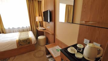 Une chambre d’hôtel équipée d’un lit, d’une télévision, d’un miroir, d’un bureau avec une tasse, d’une bouilloire et d’un plateau.