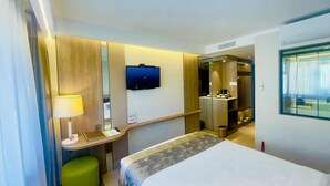 Una habitación de hotel con una cama, un escritorio con lámpara, un televisor y un espejo.