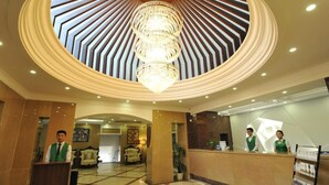 Un hall de hotel con una lámpara central, una recepción y una zona de estar con sillones.