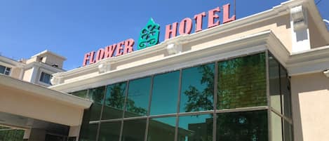 Exterior del Hotel Flower con una vista clara de la entrada y grandes ventanales que reflejan el entorno.