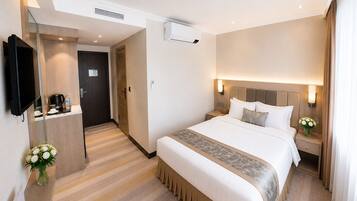 A hotel room with a large bed, bedside tables, a TV, an air conditioning unit, and a small bathroom.