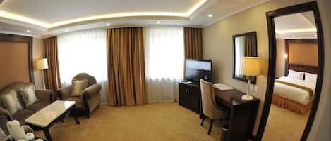 A hotel room with a sofa, armchair, desk, TV, and a bed.
