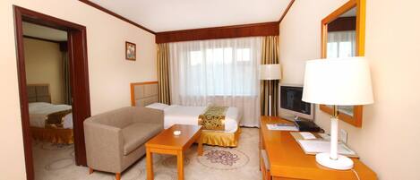 A hotel room with a bed, a sofa, a desk with a lamp, a TV, and a mirror.