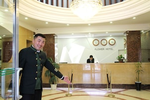 Uma área de recepção de hotel, com recepcionista, um candelabro e um relógio na parede.