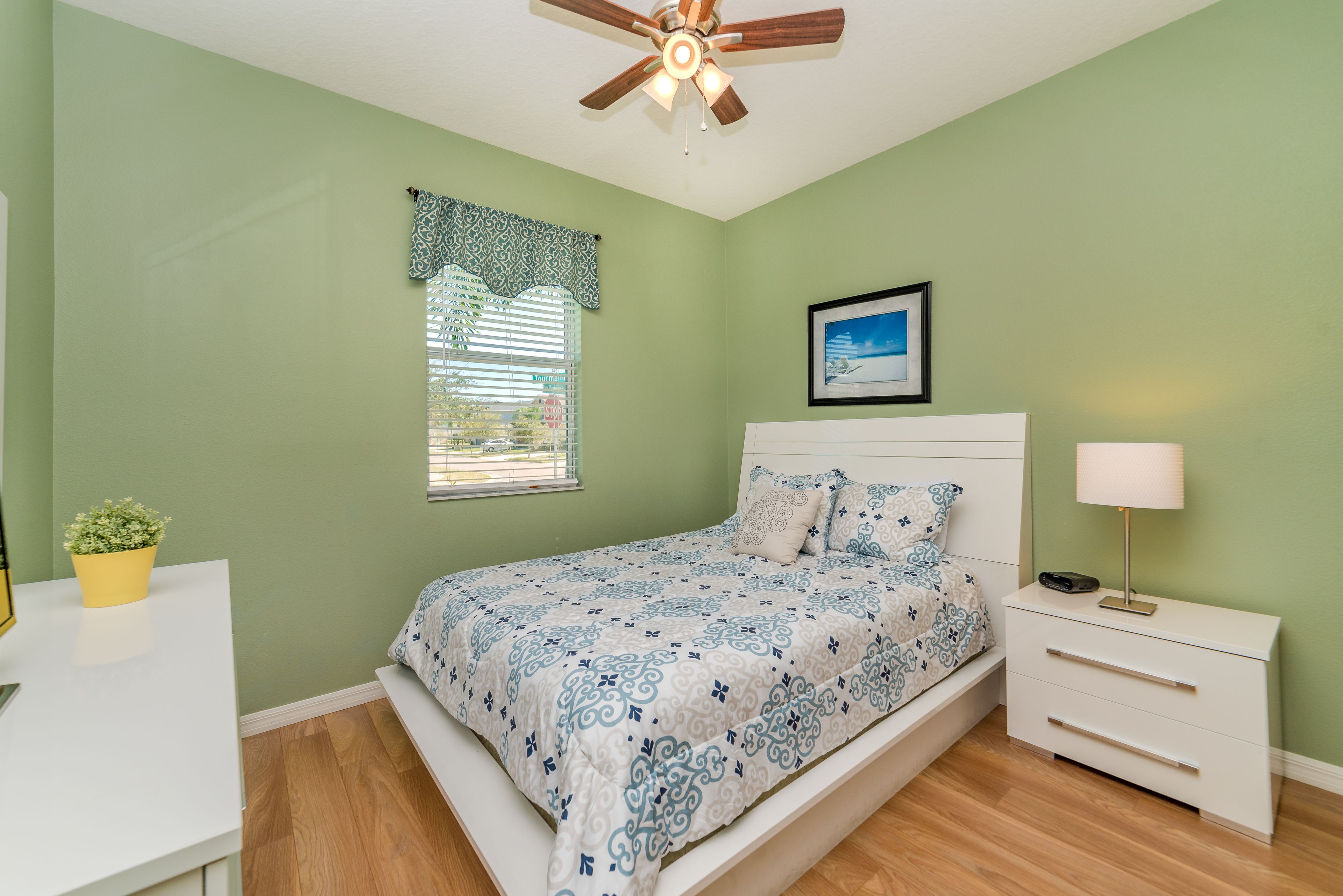 Une chambre à coucher comprenant un lit, une table de chevet, une commode et un ventilateur de plafond.