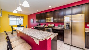 A modern kitchen with dark cabinets, a stainless steel refrigerator, a microwave, and a granite countertop island with bar stools. - Shv1189ha - 7 Bedroom Villa In Crystal Cove, Sleeps Up To 16, Just 6 Miles To Disney (Kissimmee)