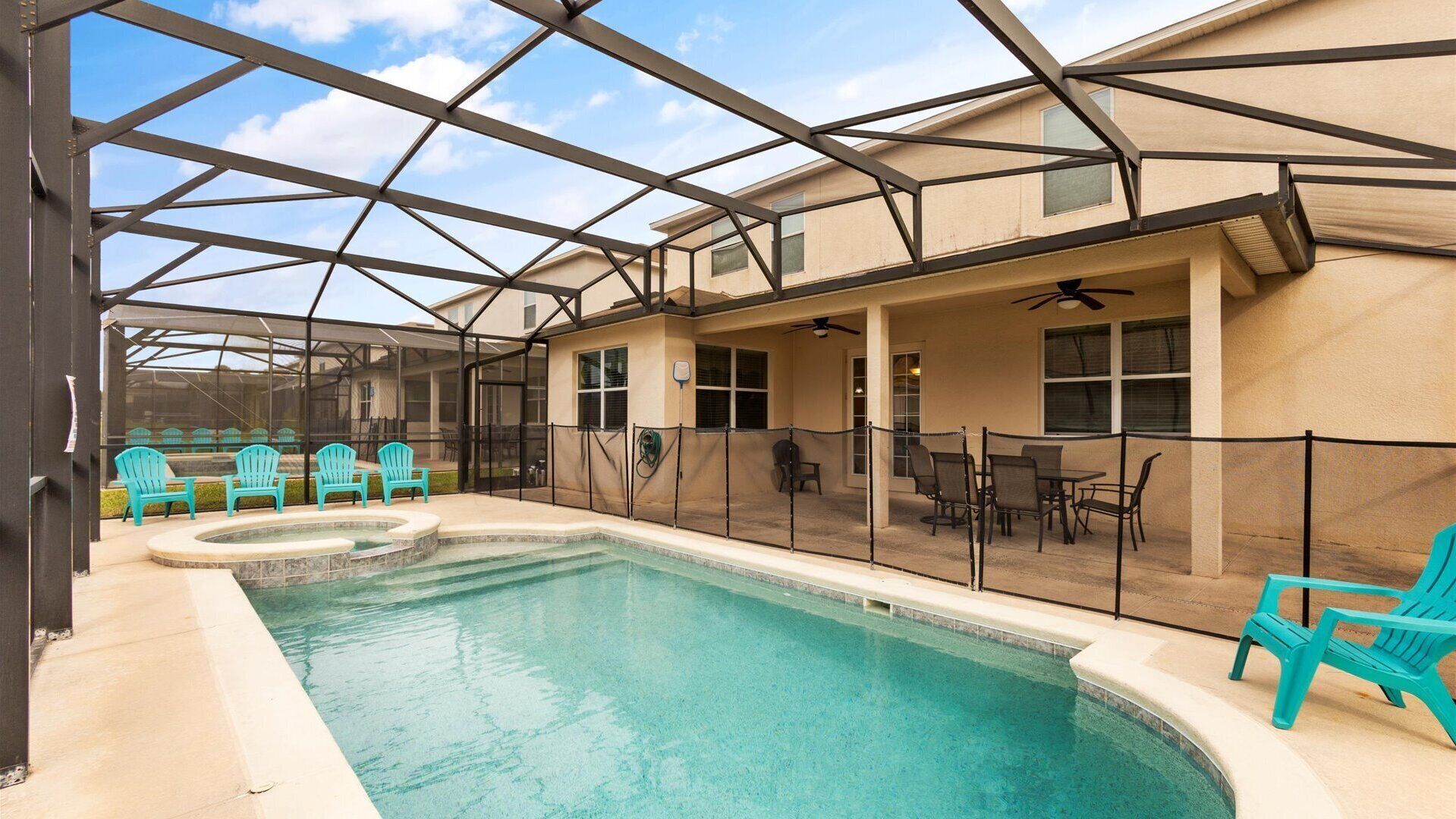 A covered outdoor swimming pool with turquoise chairs and tables, surrounded by a metal fence.
