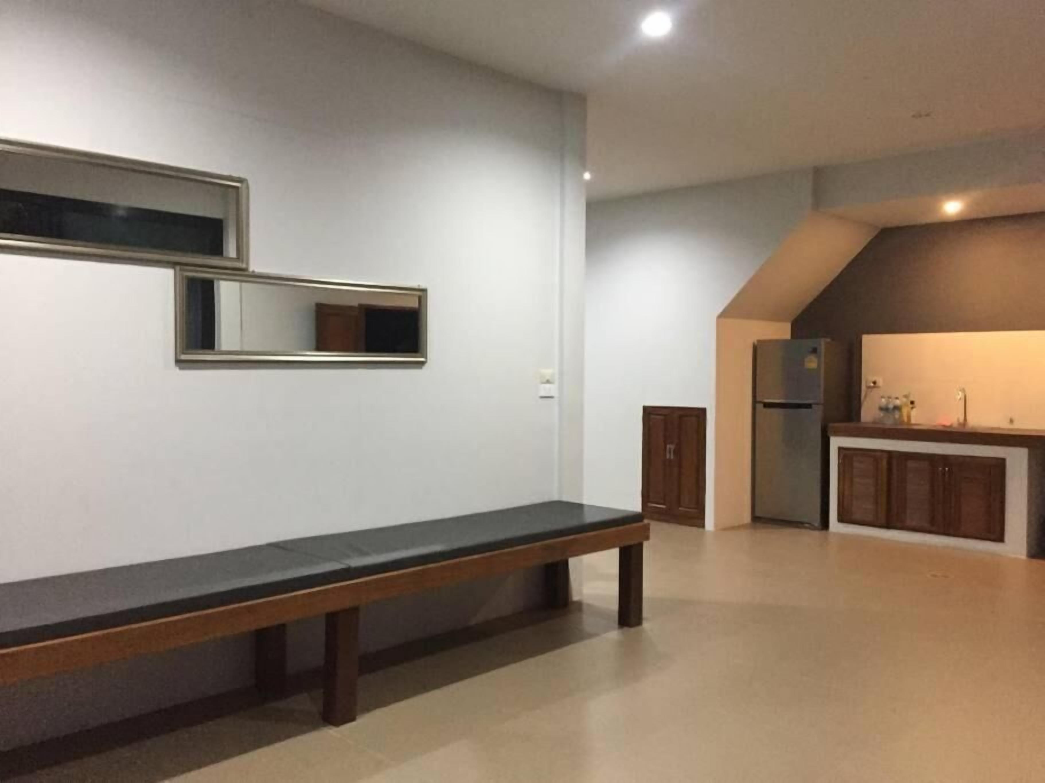 Une pièce comprenant un banc, un coin cuisine avec des placards et un miroir fixé au mur.