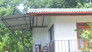Un edificio con un balcón cubierto, una puerta de madera y una ventana que da a la vegetación circundante.