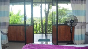 Una habitación con balcón, una cama, un ventilador de pie y cortinas.