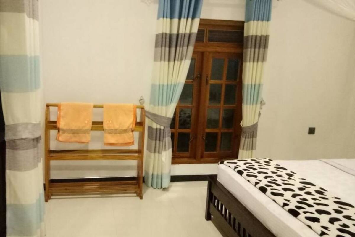 Un dormitorio con cama, un estante de madera con toallas, una ventana con cortinas y una puerta.