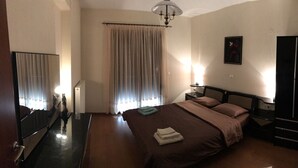 Una habitación de hotel con cama, mesitas de noche, armario, espejo y ventana con cortinas.