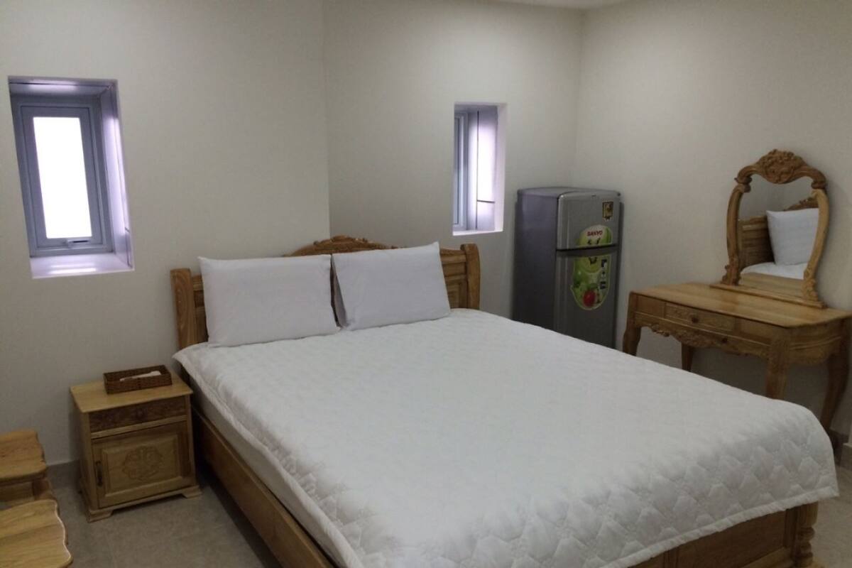 Een slaapkamer met een houten bed, twee nachtkastjes, een dressoir en een koelkast.