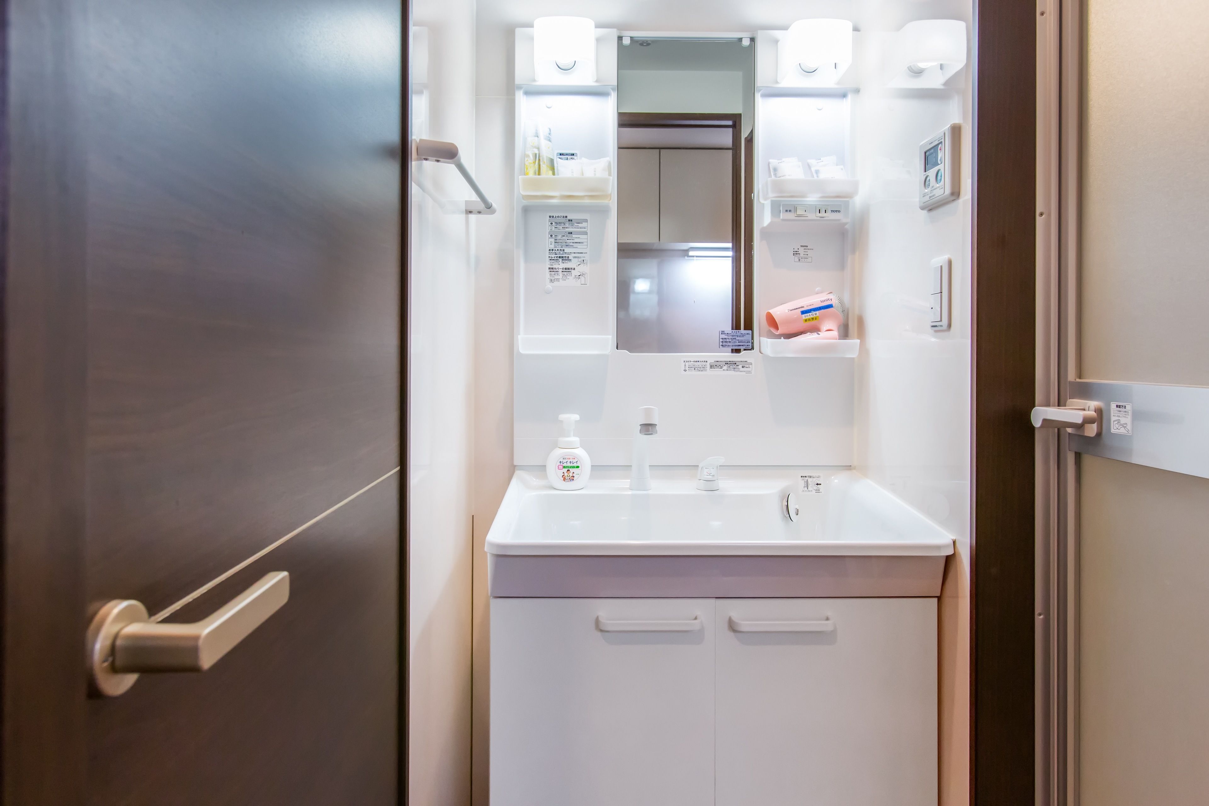 Une salle de bain avec un lavabo blanc, un miroir et une porte.