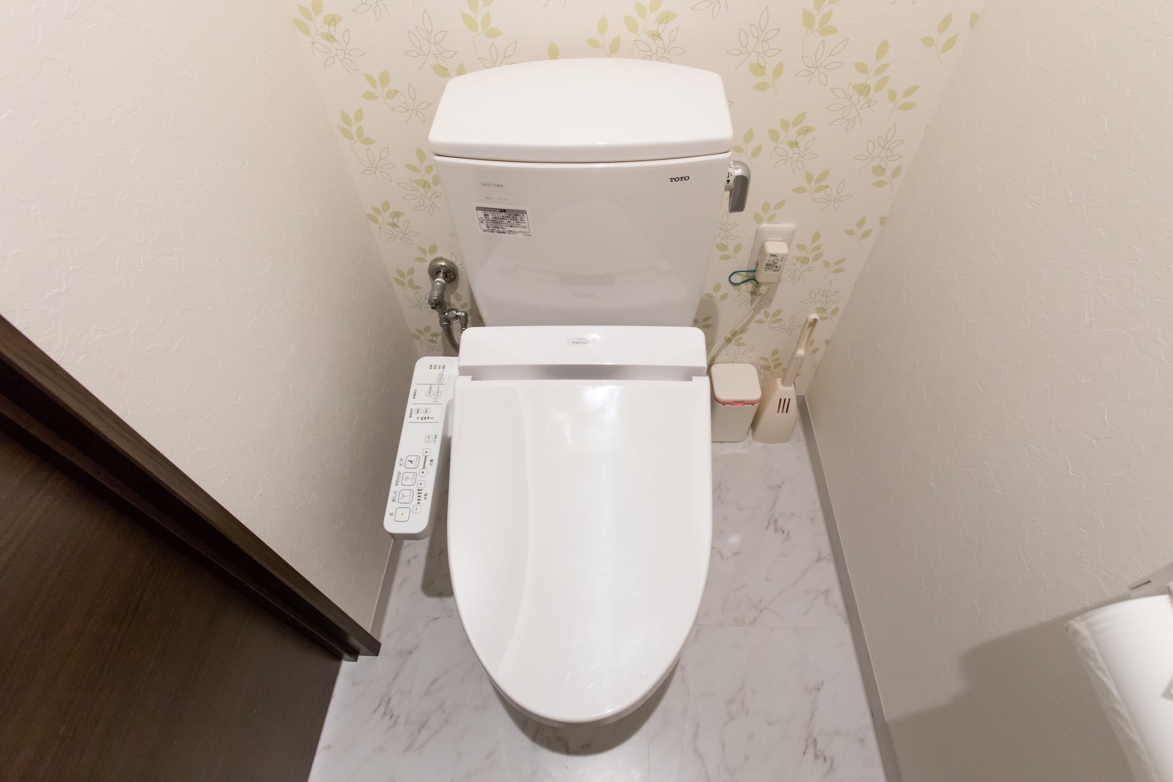A toilet with a control panel, a toilet paper holder, and a wall with a floral pattern.