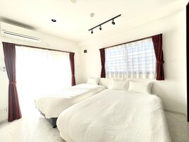 Habitación de hotel con dos camas, un ventanal con cortinas, un equipo de aire acondicionado y una lámpara empotrada en el techo.