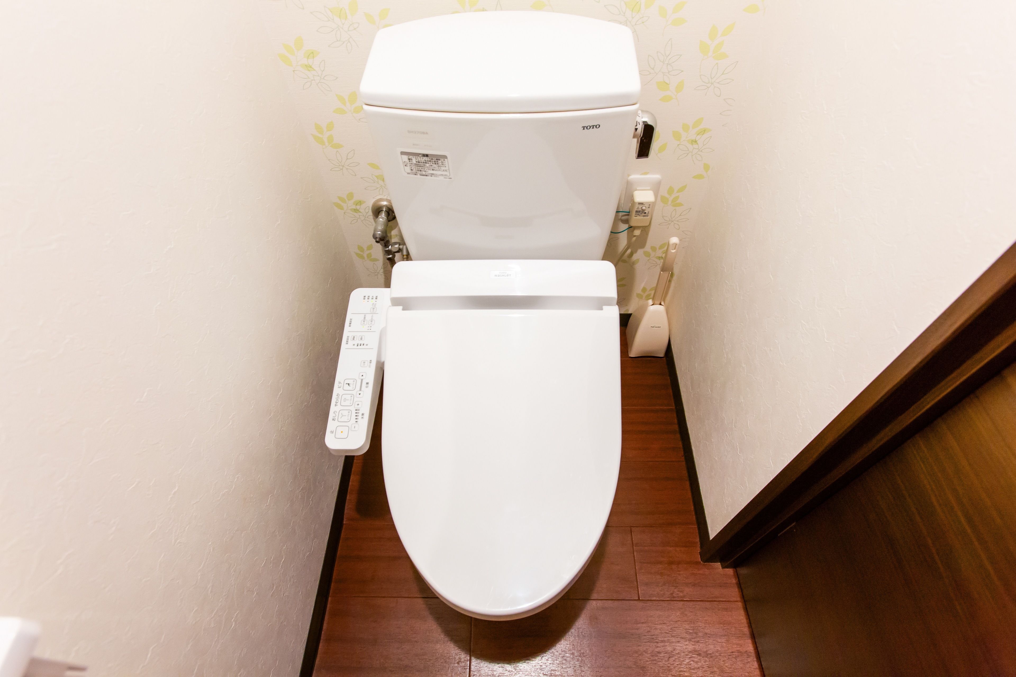 Des toilettes blanches dotées d’un panneau de commande, d’une étiquette de la marque TOTO et d’un porte-rouleau de papier toilette fixé au mur.