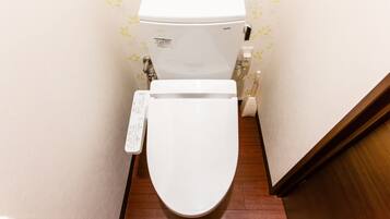 Des toilettes blanches dotées d’un panneau de commande, d’une étiquette de la marque TOTO et d’un porte-rouleau de papier toilette fixé au mur.