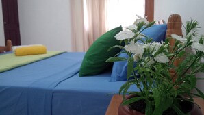 A bed with blue bedding, a green pillow, and a yellow towel. There is a potted plant with white flowers on the bed. - La Cima Kandy (Kandy)