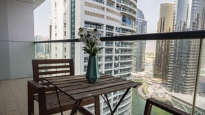 Ein Balkon mit Holztisch und -stühlen, einer Blumenvase und Blick auf moderne Hochhäuser.