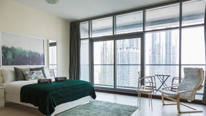 Ein modernes Schlafzimmer mit großem Fenster, einem Bett mit grüner Decke, einem Sessel und einem kleinen Tisch.
