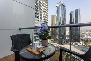 A balcony with a table set for two, a potted plant, and a view of modern high-rise buildings.