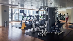Ein Fitnessstudio mit Laufbändern, Krafttrainingsgeräten und einem großen Fenster mit Blick auf eine Stadtlandschaft.