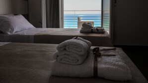 Habitación de hotel con dos camas, vista al mar y toallas sobre ellas.