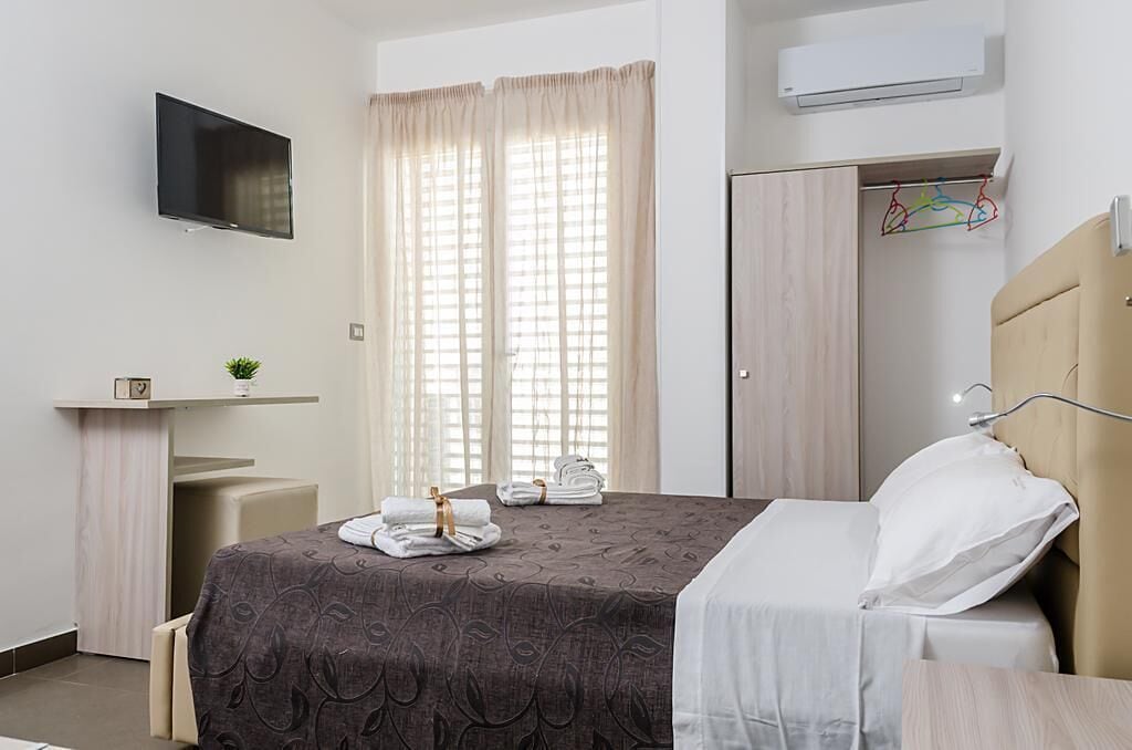 Habitació d'hotel amb un llit, televisió penjada a la paret, un armari i una petita taula de nit amb una planta.