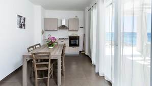Una cocina moderna con armarios de madera, una mesa de comedor con sillas y vistas al mar a través de amplios ventanales.