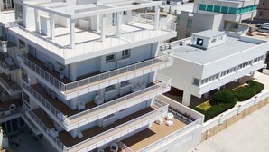 Un edificio residencial de varios pisos con balcones, una terraza en la azotea y un pequeño jardín.