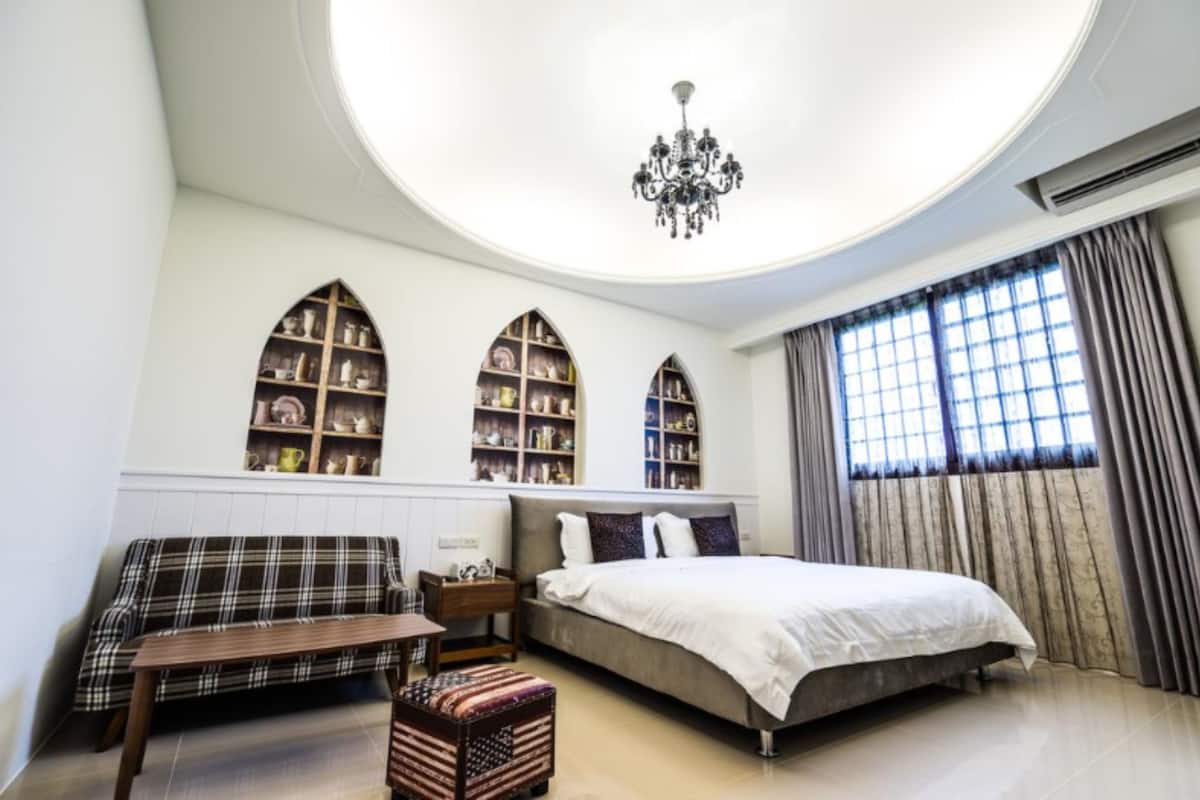 Un dormitorio con cama, sofá, una mesita y un banco. Se observan tres estanterías contra la pared.