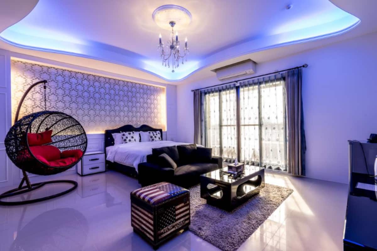 Un dormitorio moderno con cama, una silla colgante, una mesita de centro y un gran ventanal con cortinas.