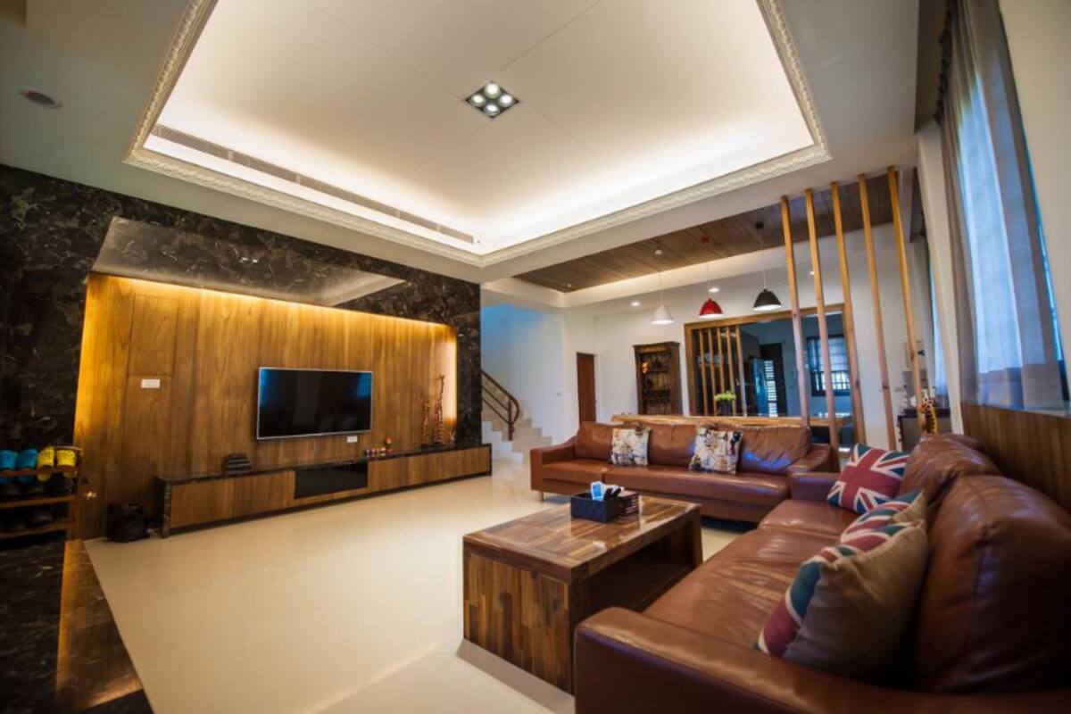 Una sala de estar moderna con un televisor de pantalla plana grande, paneles de madera, un sofá de cuero y una mesa de centro.