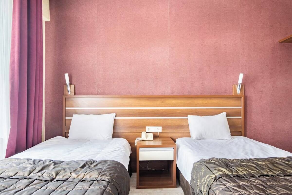 A double room with two beds, a wooden headboard, bedside tables with lamps, and a red wall.