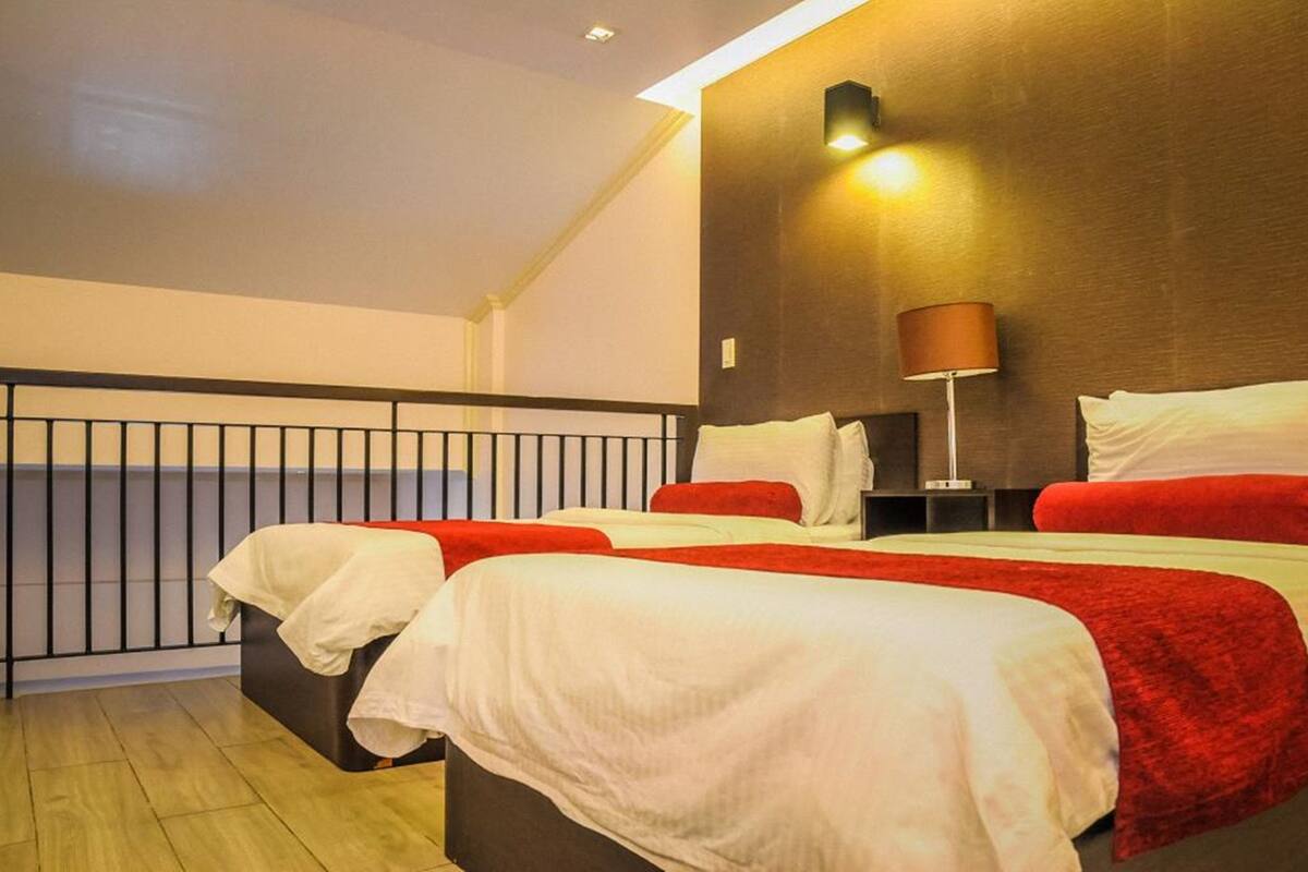Une chambre d’hôtel avec deux lits, un balcon, une lampe fixée au mur et un plancher en bois.