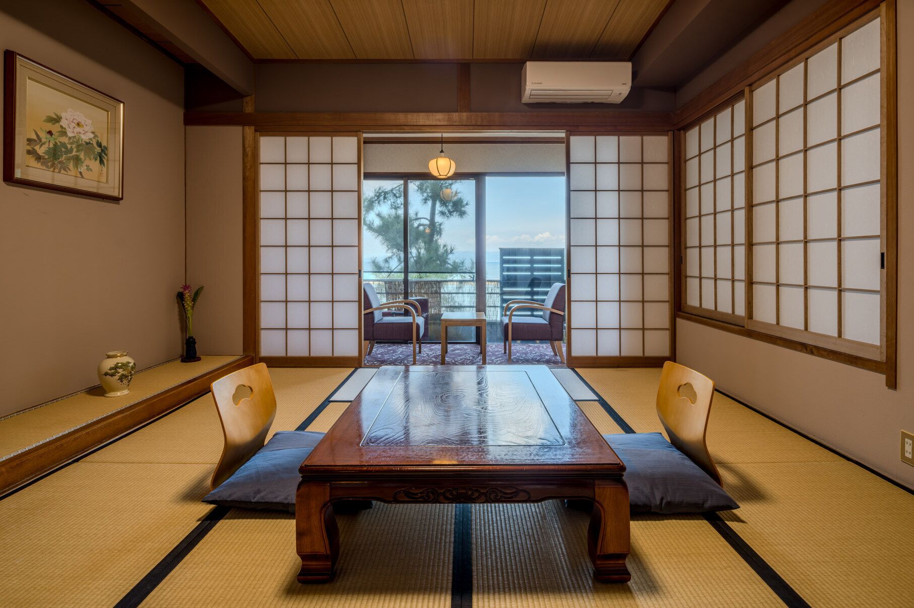 Et traditionelt japansk rum med tatamimåtter, et lavt bord, to stole, en shoji-skærm og udsigt til naturen.