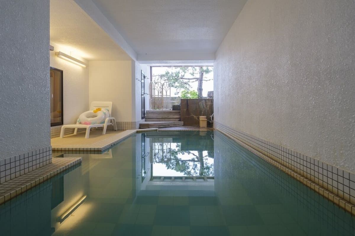 An indoor swimming pool with a tiled edge, a lounge chair, and a staircase leading to an outdoor area.